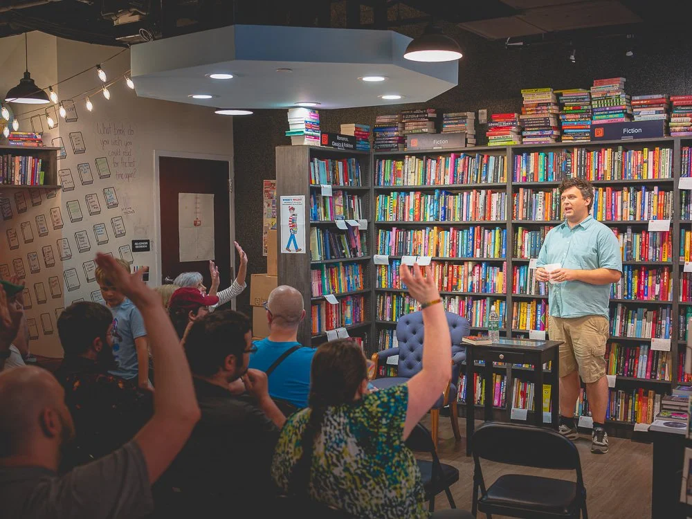 A Prologue Bookshop host speaking with hands raised in the audience