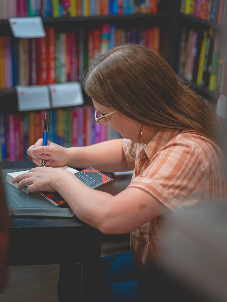 Bonnie Quinn signing a copy of her book against a wall of colorful titles