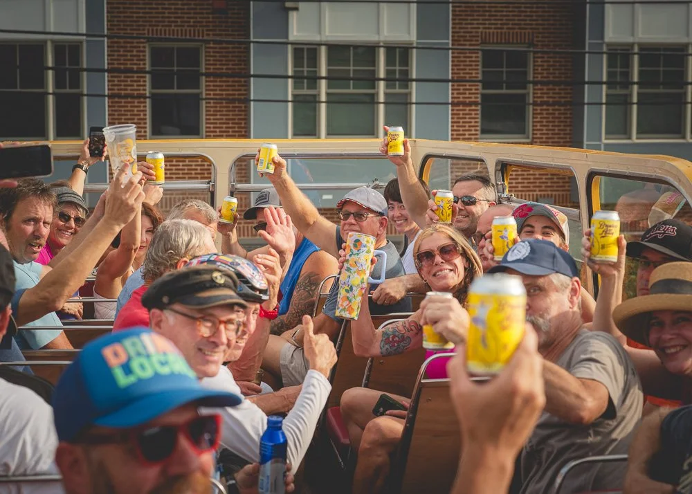 Spectators on an open-air bus raising drinks in a celebratory toast