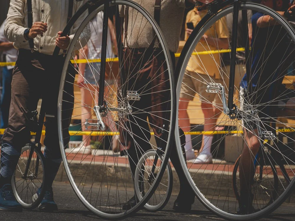 Close view of high-wheel bicycle wheels and riders waiting at street level