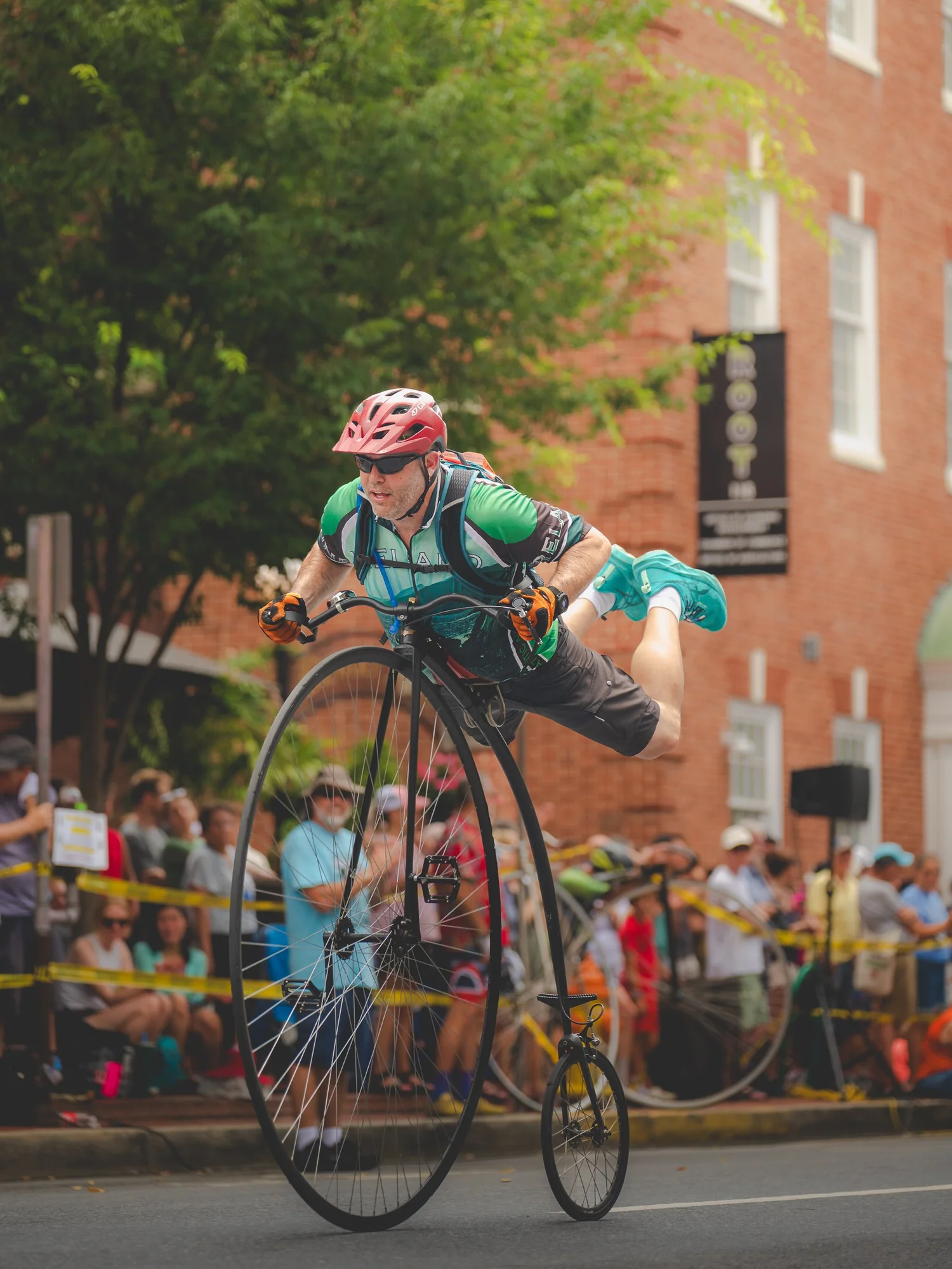 A cyclist performing a one-legged balance on a high-wheel bicycle