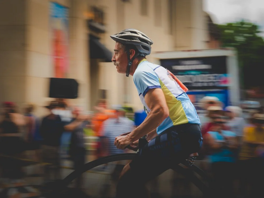A high-wheel cyclist racing past the crowd with the background in motion blur