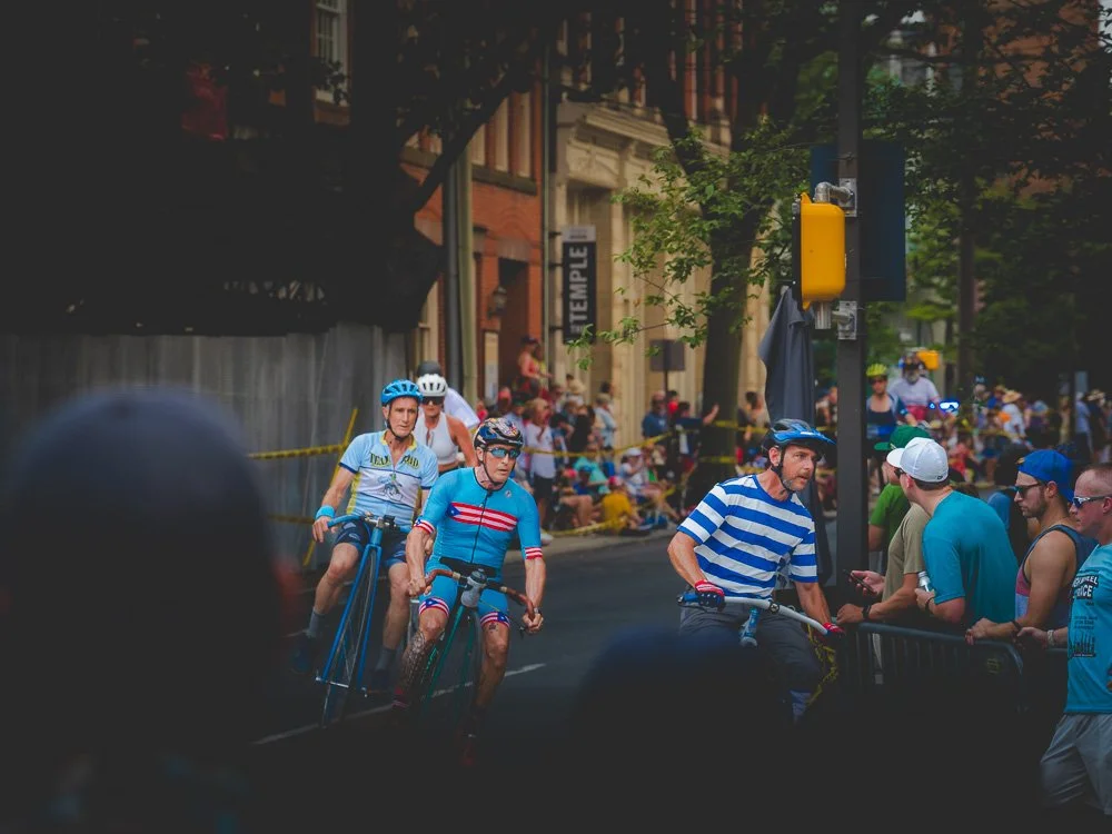High-wheel cyclists rounding a corner through the crowd