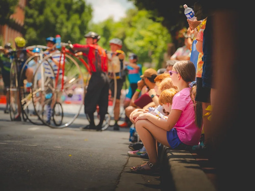 A young spectator watching racers prepare on the sunlit street