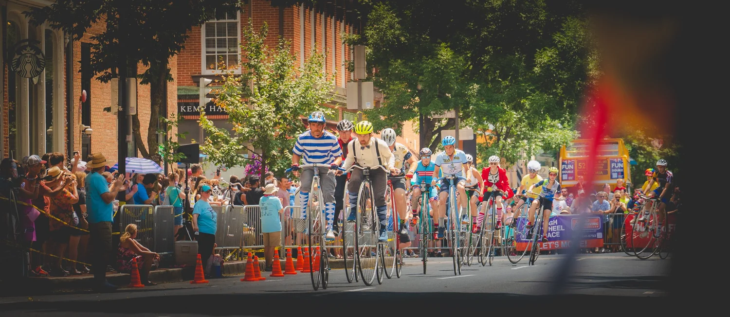 High-wheel bicycle racers riding toward the camera through downtown Frederick, Maryland