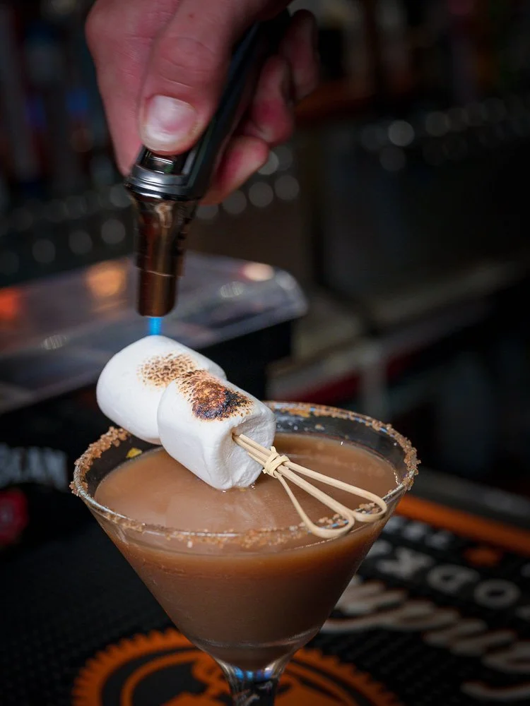 A bartender toasting marshmallows over a dessert cocktail