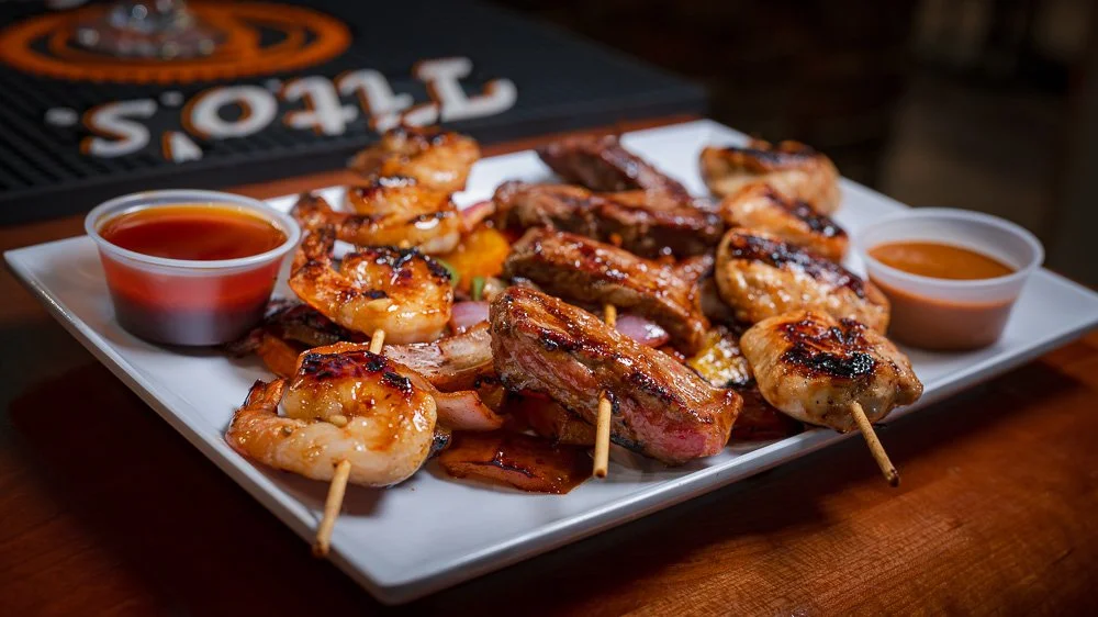 A platter of grilled steak and chicken skewers with dipping sauces