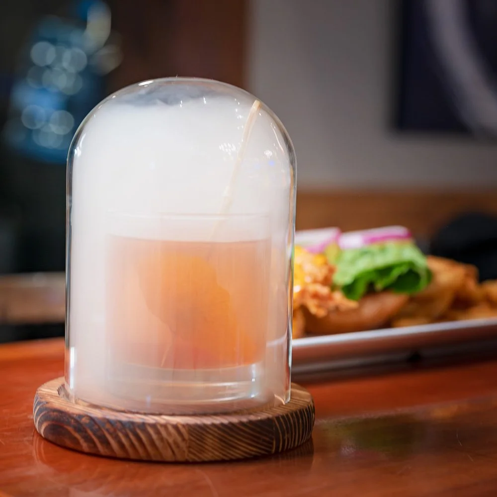 A smoked cocktail sealed beneath a glass dome