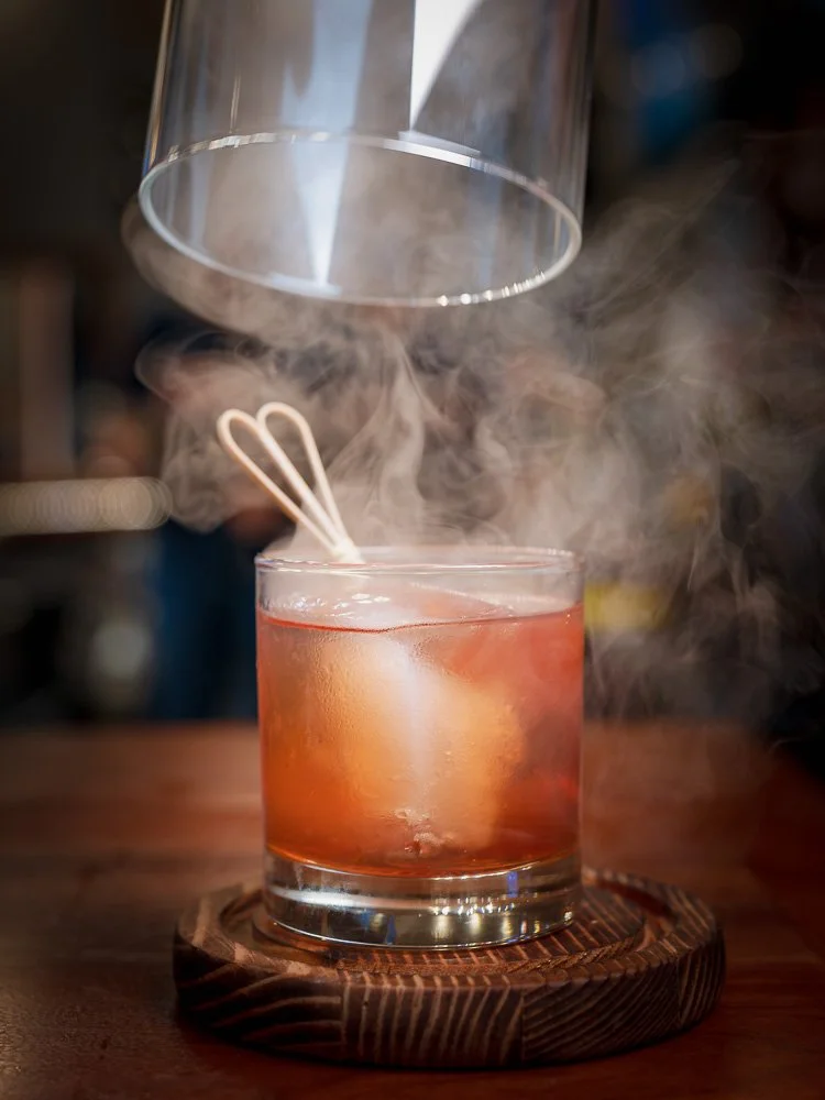 Smoke curling around Liberty Social's signature Old Fashioned