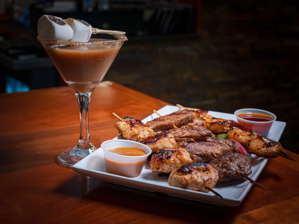 Toasted marshmallow cocktail beside grilled steak and chicken skewers