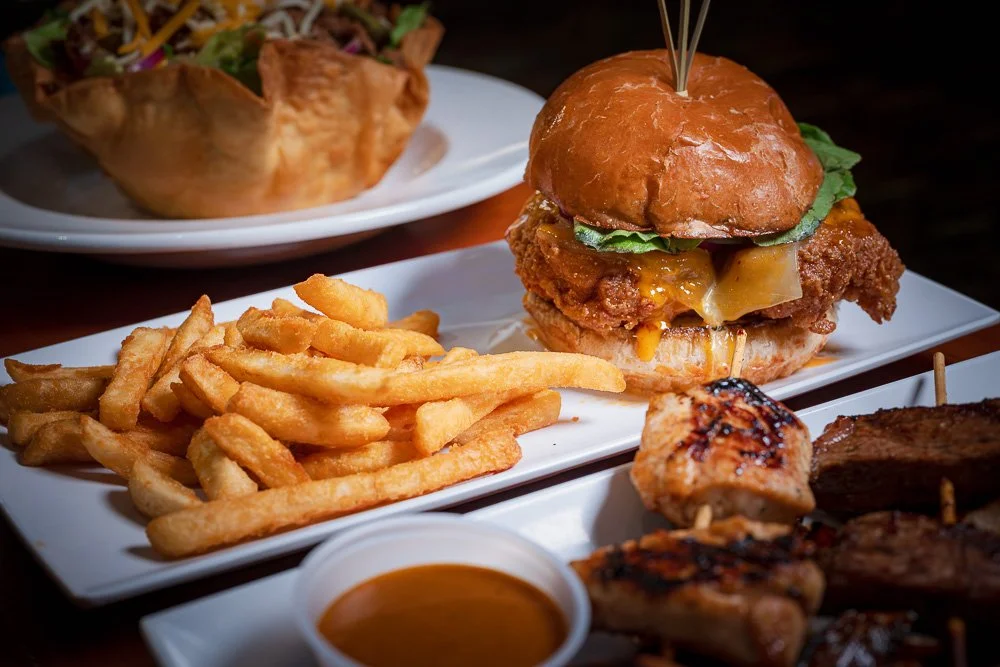 Fried chicken sandwich, fries, salad, and grilled skewers spread across a table
