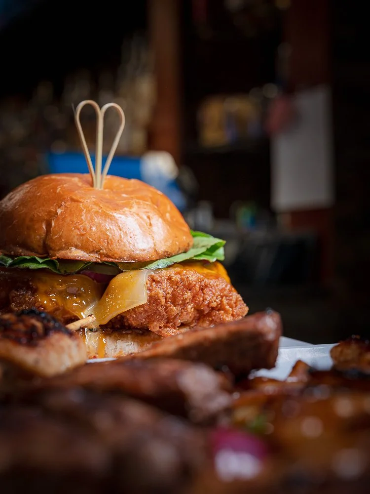 Fried chicken sandwich framed behind a platter of grilled skewers